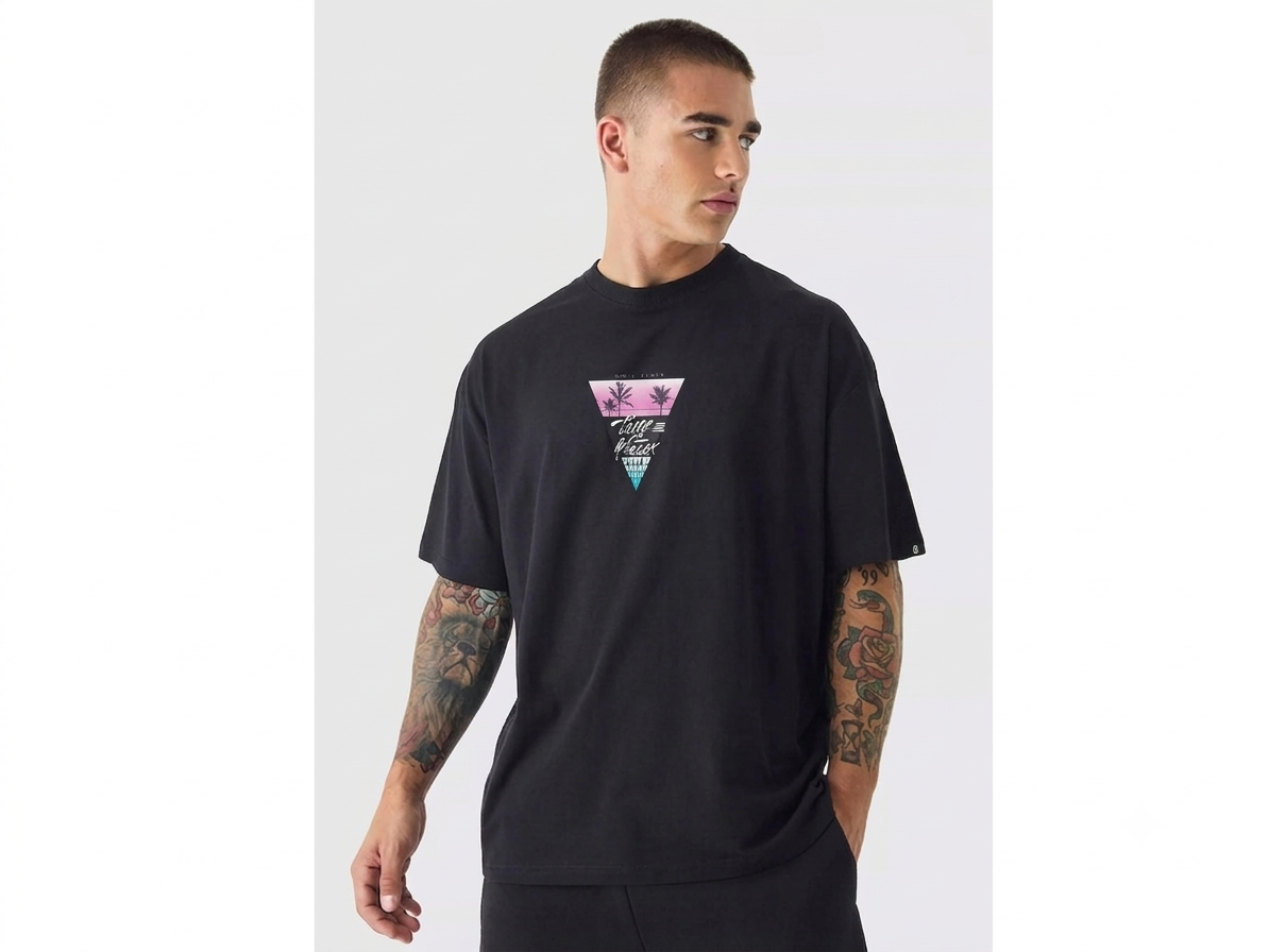 A man wearing a black short-sleeve t-shirt with a colorful geometric graphic on the chest, photographed against a light gray studio background.