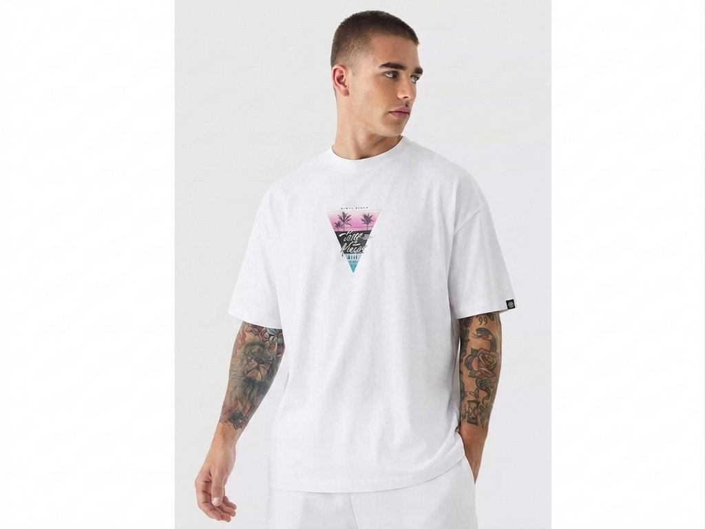 A man wearing a white short-sleeve t-shirt with a colorful geometric triangle graphic on the chest, set against a plain light gray studio background.