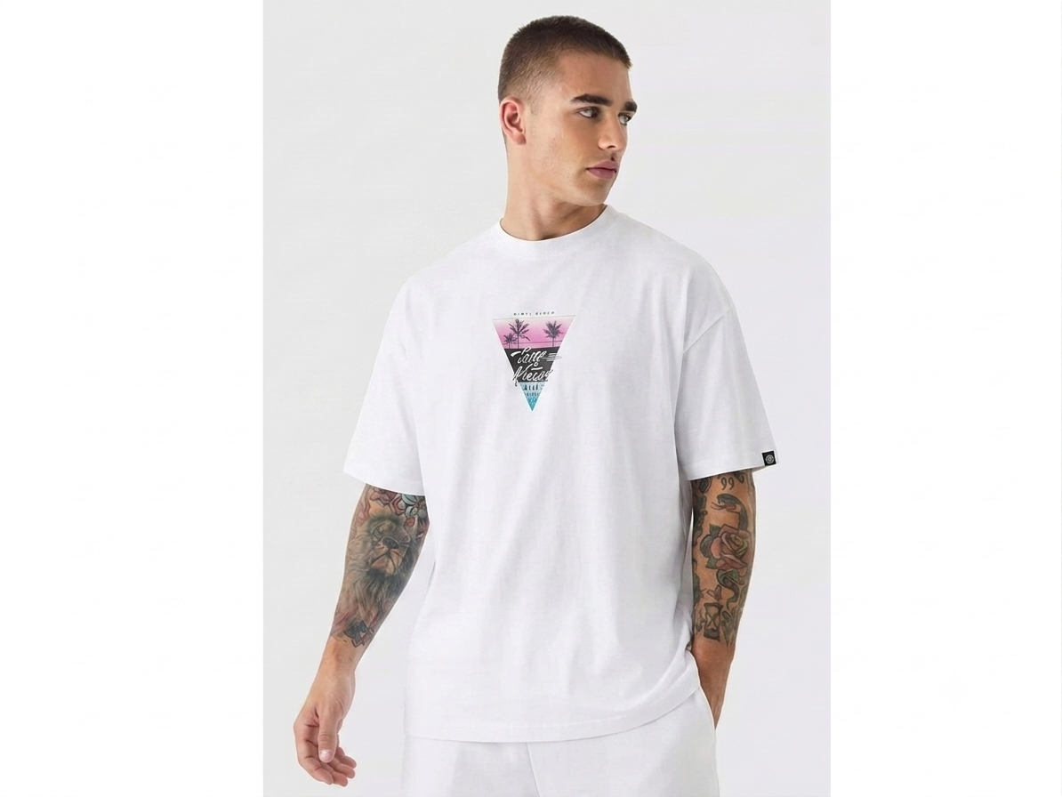 A man wearing a white short-sleeve t-shirt with a colorful geometric triangle graphic on the chest, set against a plain light gray studio background.