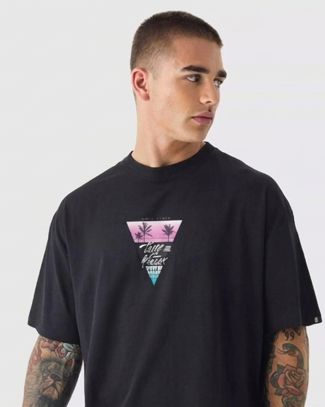 A man wearing a black crewneck t-shirt with a pink and blue graphic on the chest, photographed against a light gray background.