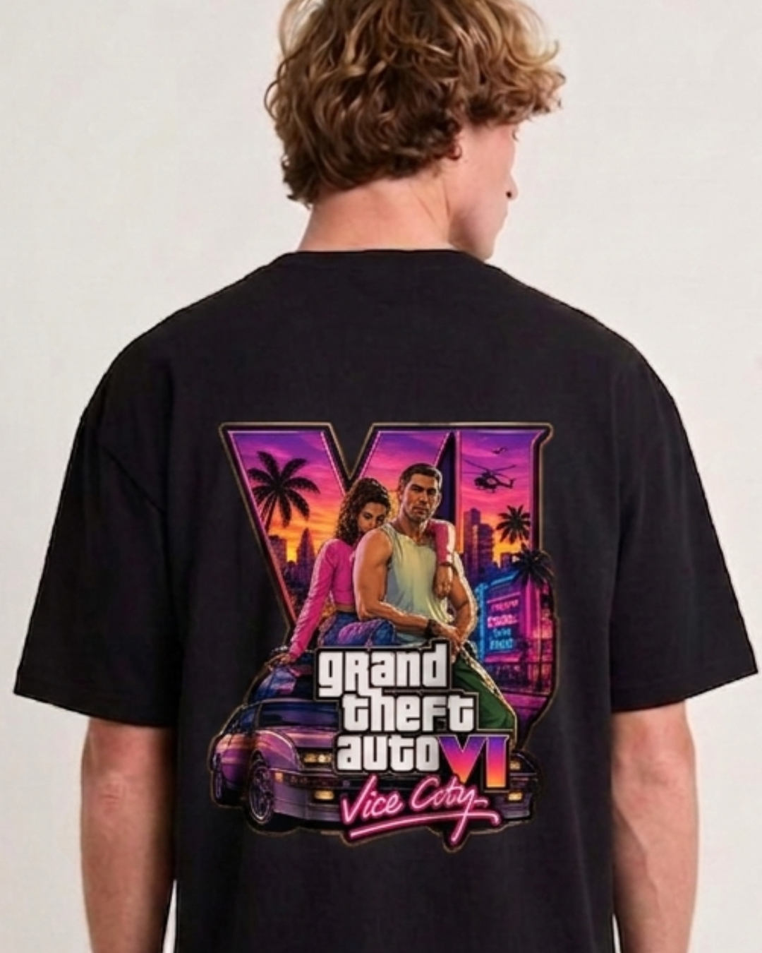 A man wearing a black t-shirt, viewed from the back. The shirt features a large graphic print of the video game Grand Theft Auto VI, showing characters and the game's logo in vibrant neon colors over a sunset cityscape.